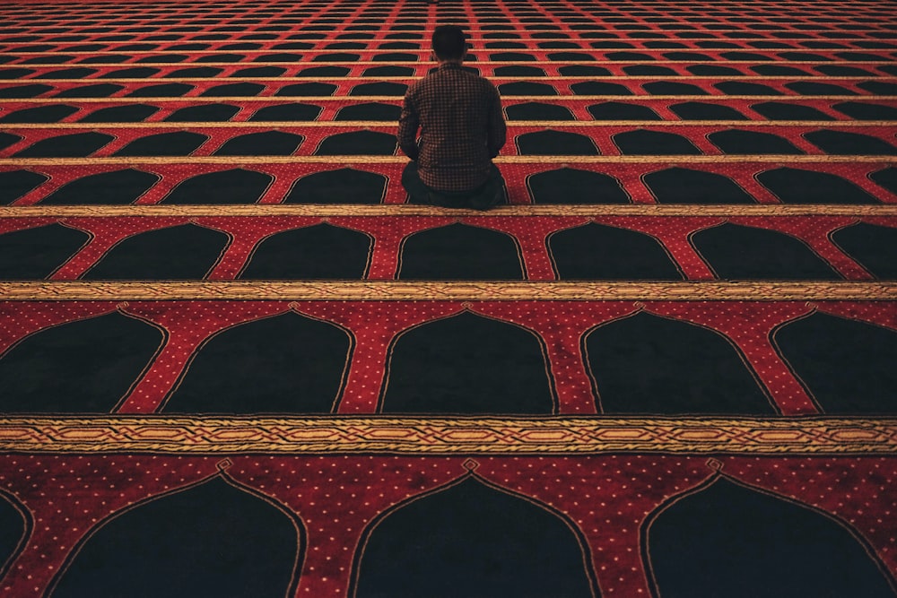 man in red shirt kneeling on red and black carpeted floor