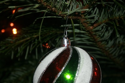 Close-up of shimmering ornaments hanging delicately from pine branches, reflecting soft holiday lights.