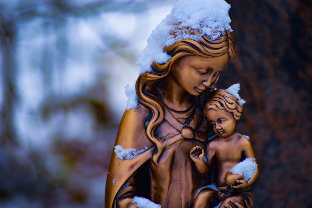 Statue brune de la mère et de l’enfant partiellement recouverte de neige