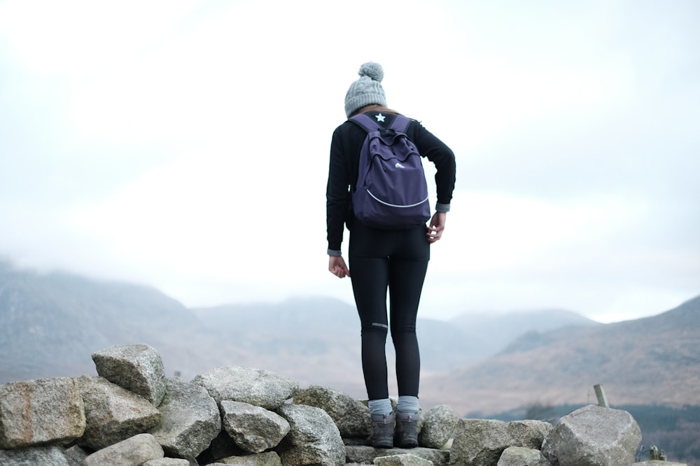 woman standing on gray rock while wearing blue backpack