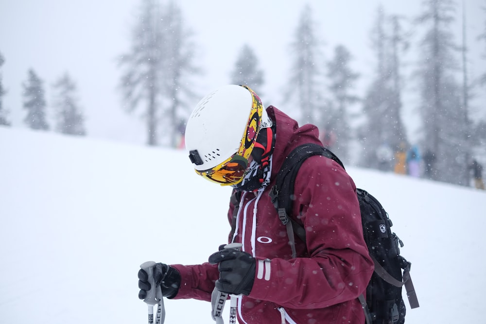 Mann mit lila Jacke und Helm hält Skistöcke auf schneebedecktem Feld
