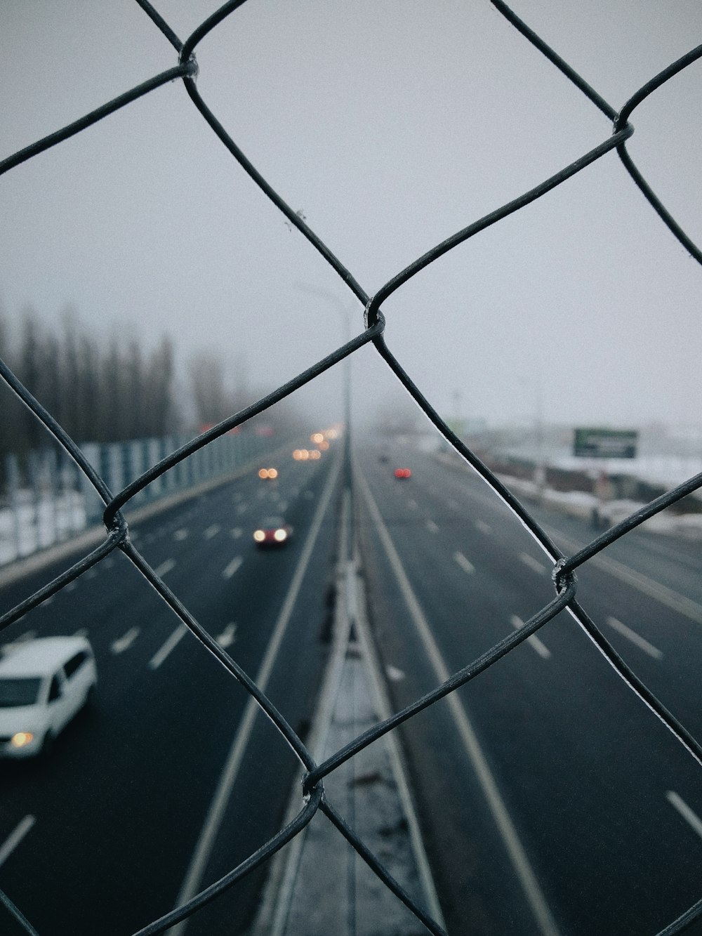 gray metal wire-link fence overlooking highway with passing cars