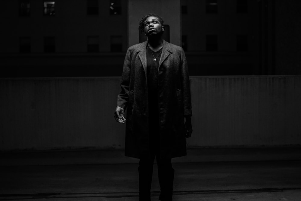 grayscale photography of man standing wearing coat