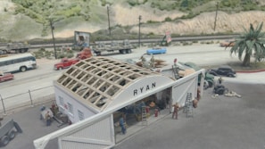 A detailed diorama depicting a construction scene, featuring people working on a building with a partially constructed roof. The structure has the name 'RYAN' on it. There are various vehicles and trees in the background, as well as a road with cars and a bus. The environment includes a mountainous terrain and a railway track along the road.