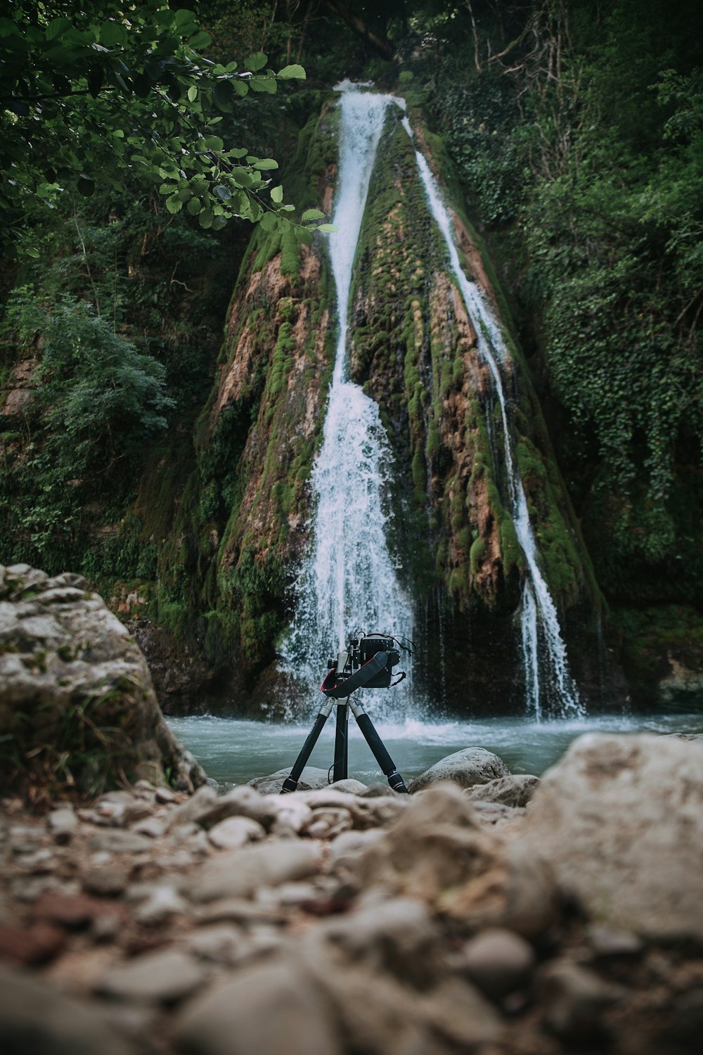 tripod on rocky shore with waterfall background