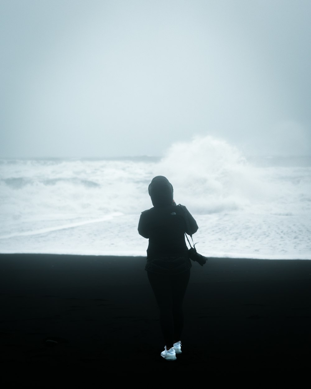 man wearing jacket with camera standing in front of ocean waves