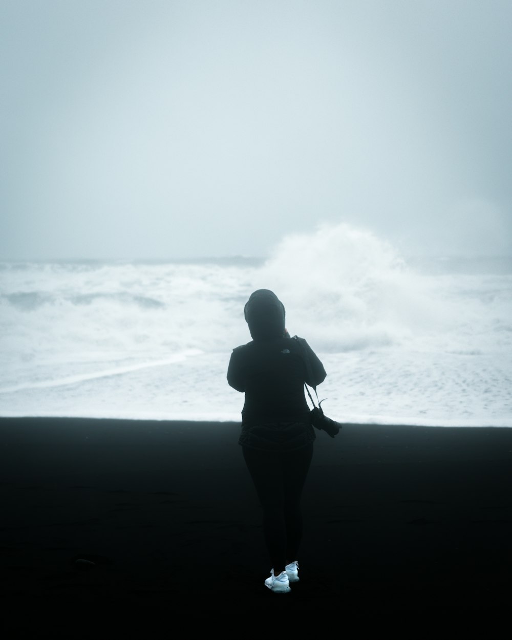 海の波の前に立つカメラを持ったジャケットを着た男性
