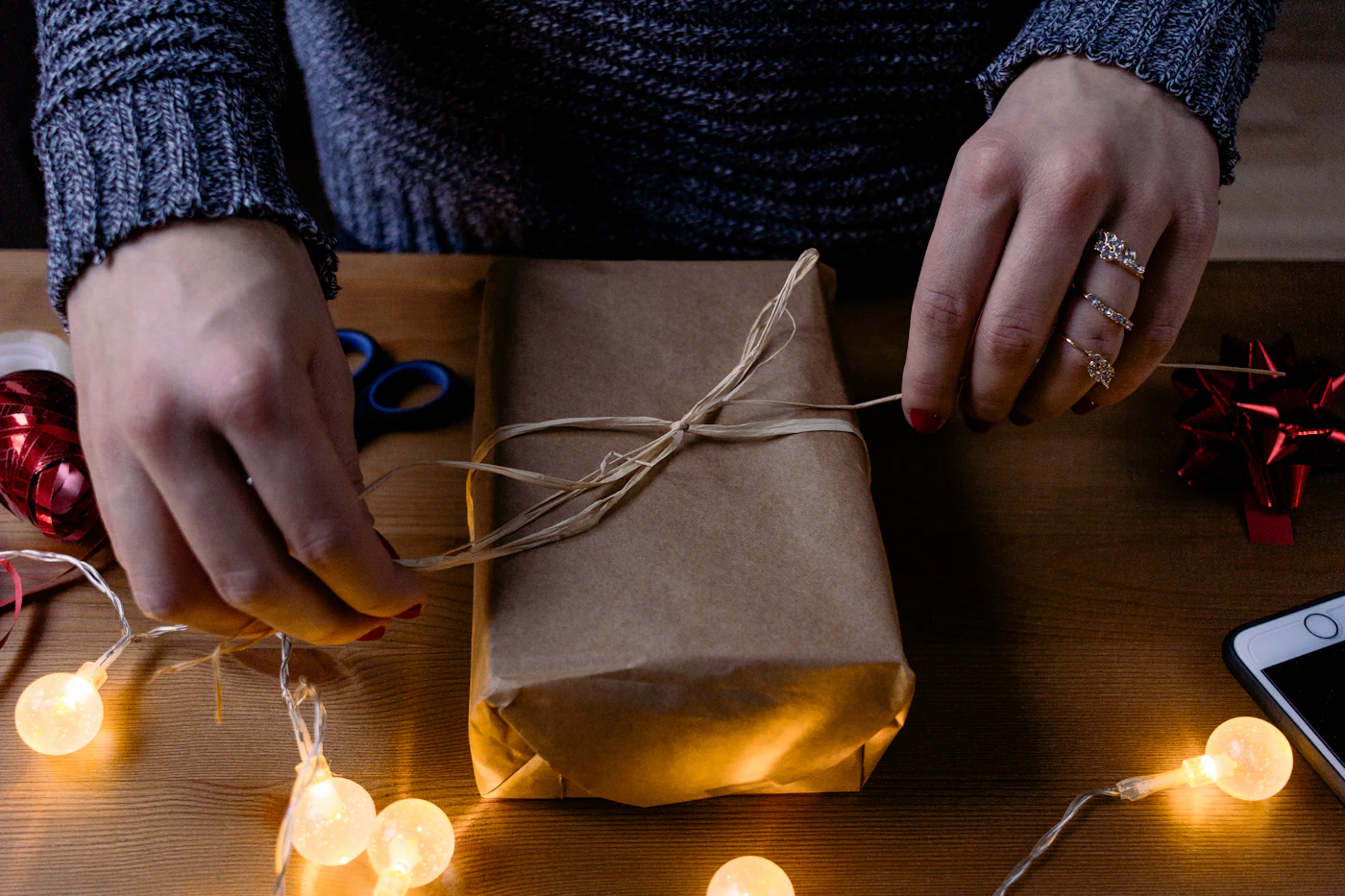 Hands carefully tying ribbon around a brown craft gift box