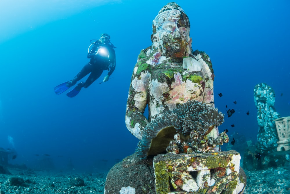 diver diving on ocean floor near statue
