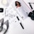 A flat lay arrangement featuring a magazine with a stylish woman in a white outfit, surrounded by a black and white striped pair of shoes, a pair of glasses, a watch, a camera lens, makeup items, and a candle.