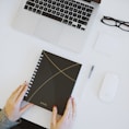 person holding notebook near laptop