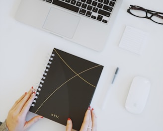 person holding notebook near laptop