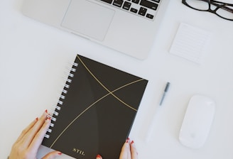 person holding notebook near laptop