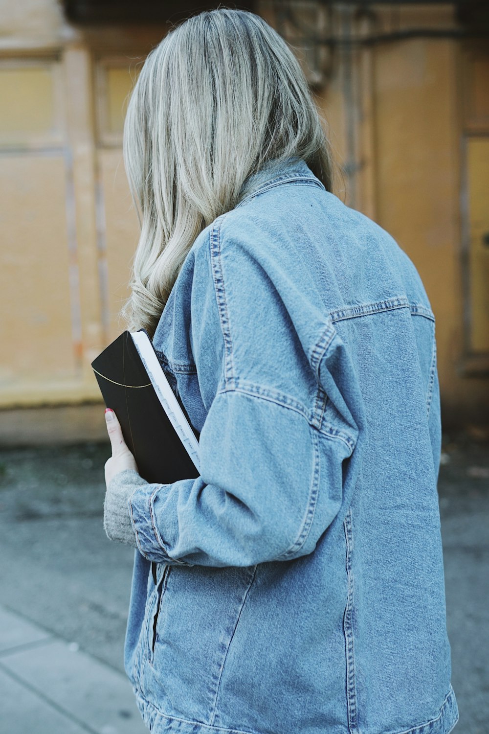 woman wearing blue denim jacket holding black book