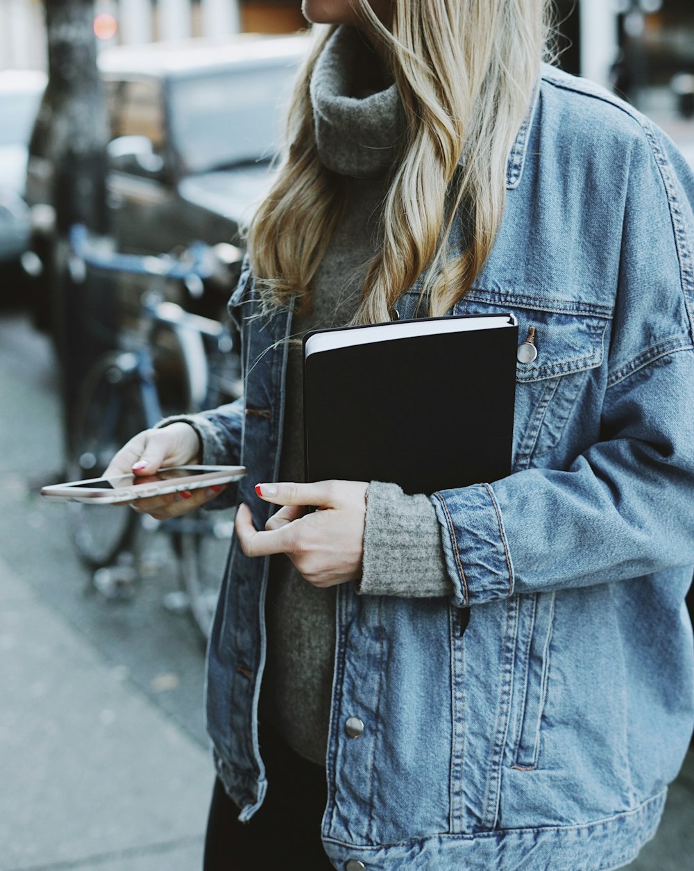 Frau steht auf dem Bürgersteig und hält Buch und Smartphone in der Hand
