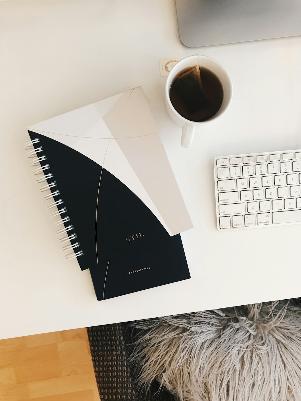 caderno espiral branco e preto perto de xícara de chá branca cheia de líquido preto