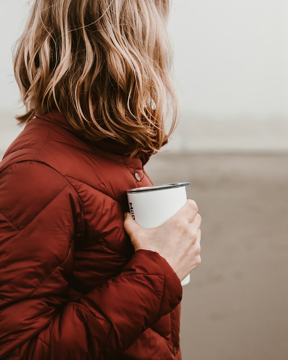 woman wearing brown bubble jacket holding white disposable cup