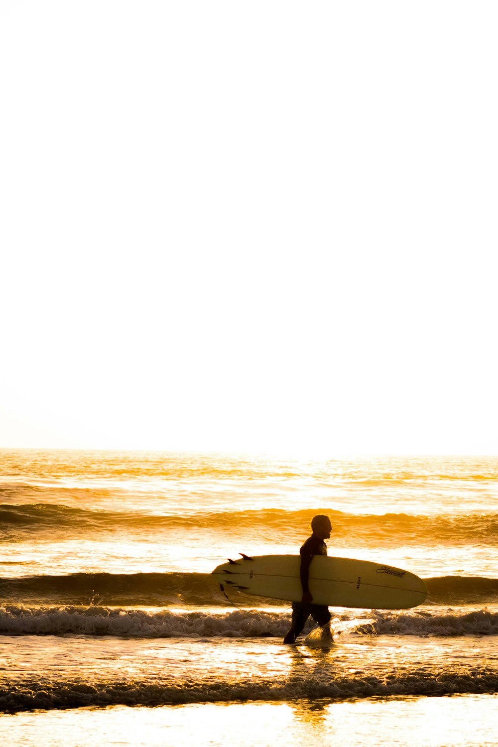 man carrying white surfboard walking on seashore