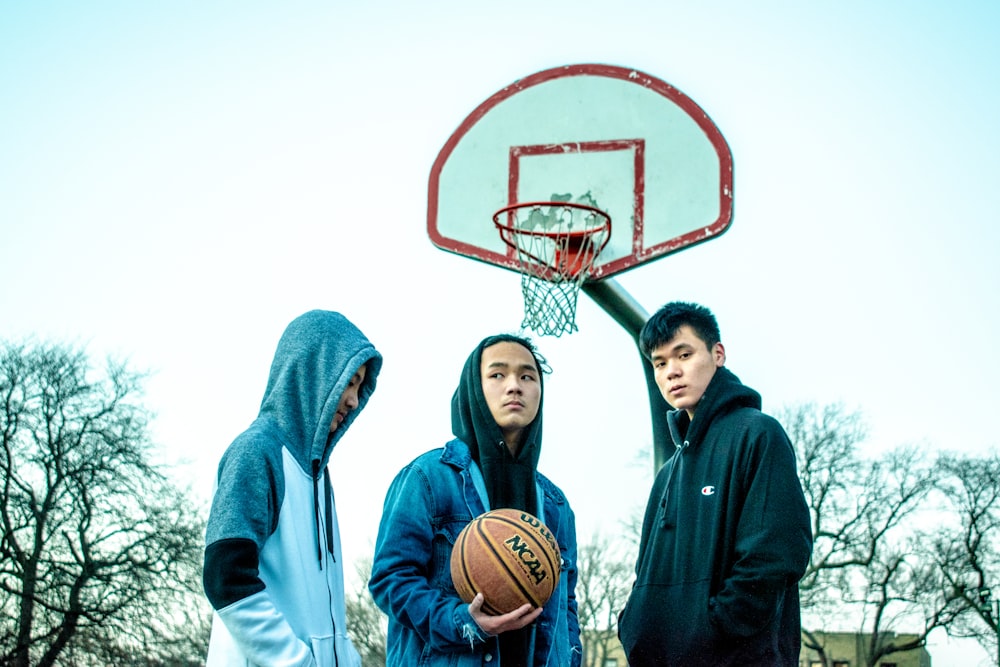 three men wearing hoodie near basketball hoop