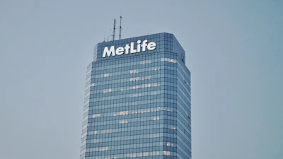 A tall, modern skyscraper with a glass facade and the word 'MetLife' displayed prominently near the top. The building has multiple floors with lights visible in some windows. The sky is clear and gives a serene backdrop to the structure.