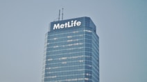 A tall, modern skyscraper with a glass facade and the word 'MetLife' displayed prominently near the top. The building has multiple floors with lights visible in some windows. The sky is clear and gives a serene backdrop to the structure.