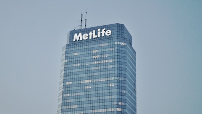 A tall, modern skyscraper with a glass facade and the word 'MetLife' displayed prominently near the top. The building has multiple floors with lights visible in some windows. The sky is clear and gives a serene backdrop to the structure.