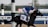 A jockey in a blue uniform rides a racehorse during a race, with the number 10 visible on the horse's harness. The background includes a racecourse with blurred spectators and palm trees.