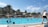 A family enjoying a sunny day by a large swimming pool surrounded by greenery.