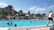 A family enjoying a sunny day by a large swimming pool surrounded by greenery.