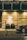 A luxurious entrance of the Grand Hyatt featuring a well-lit stone wall with a prominent logo. Two potted plants with decorative lighting are placed in front. A polished black luxury car is partially visible on the right, parked on a cobblestone road.
