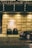 A luxurious entrance of the Grand Hyatt featuring a well-lit stone wall with a prominent logo. Two potted plants with decorative lighting are placed in front. A polished black luxury car is partially visible on the right, parked on a cobblestone road.