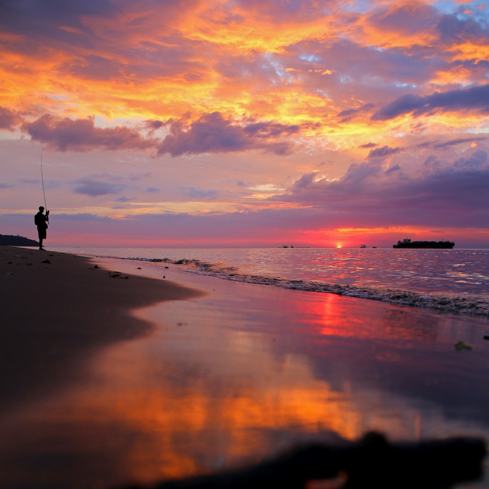 uomo in piedi sulla riva del mare durante l'ora d'oro