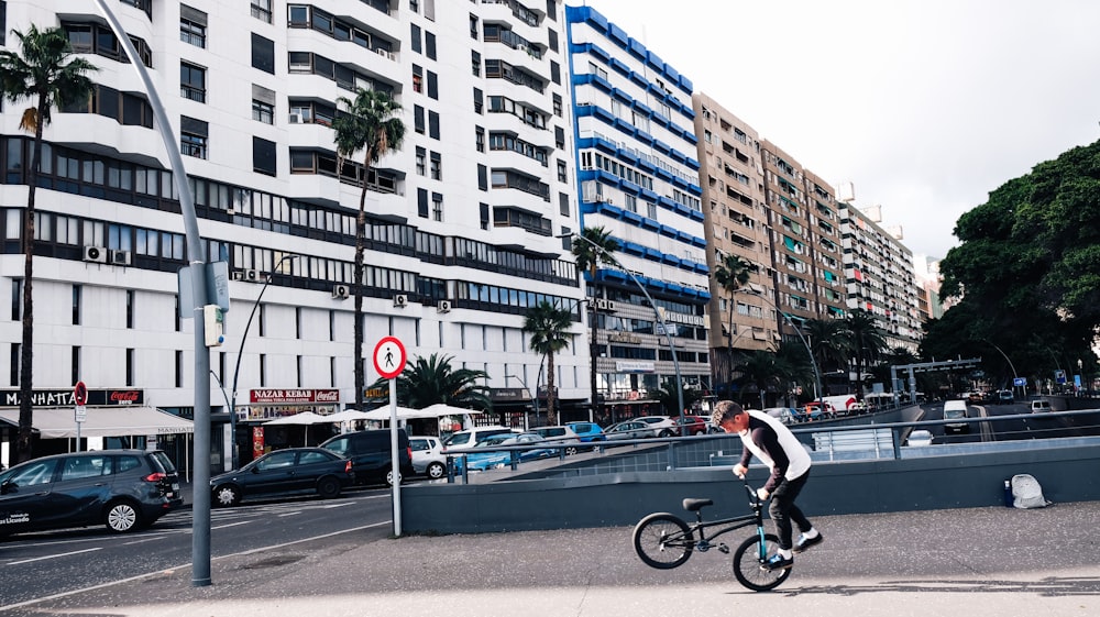 man doing tricks on a BMX bike near the road and buildings