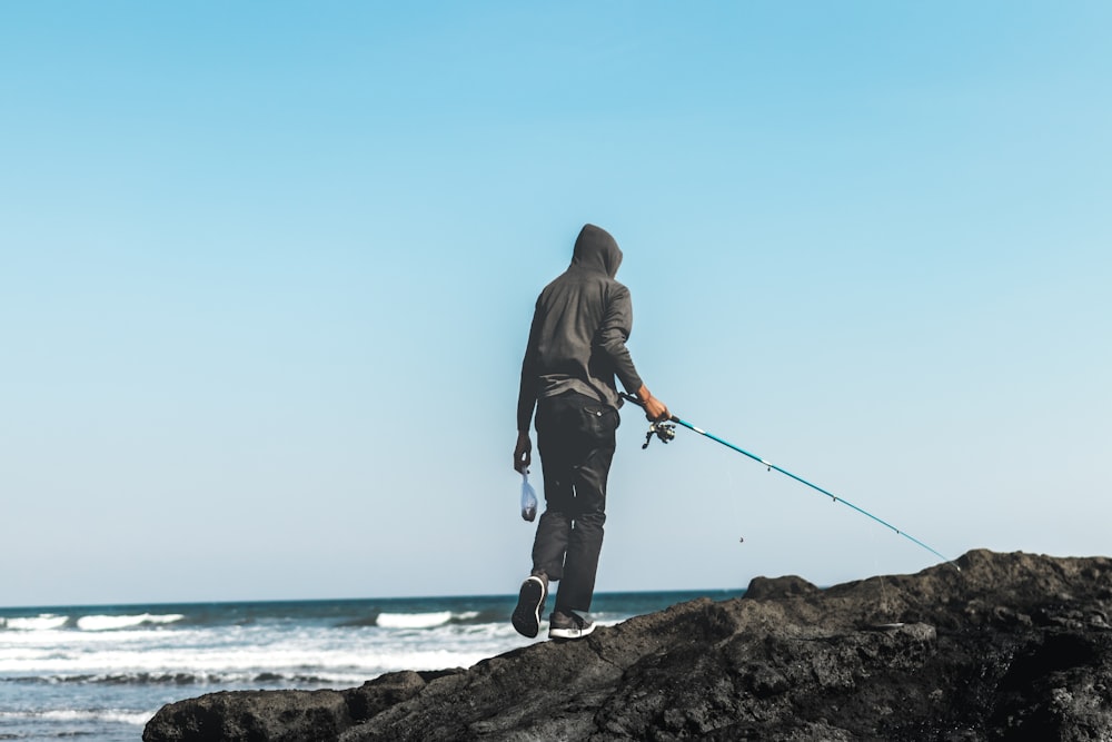 person standing on seacliff holding fishing rod