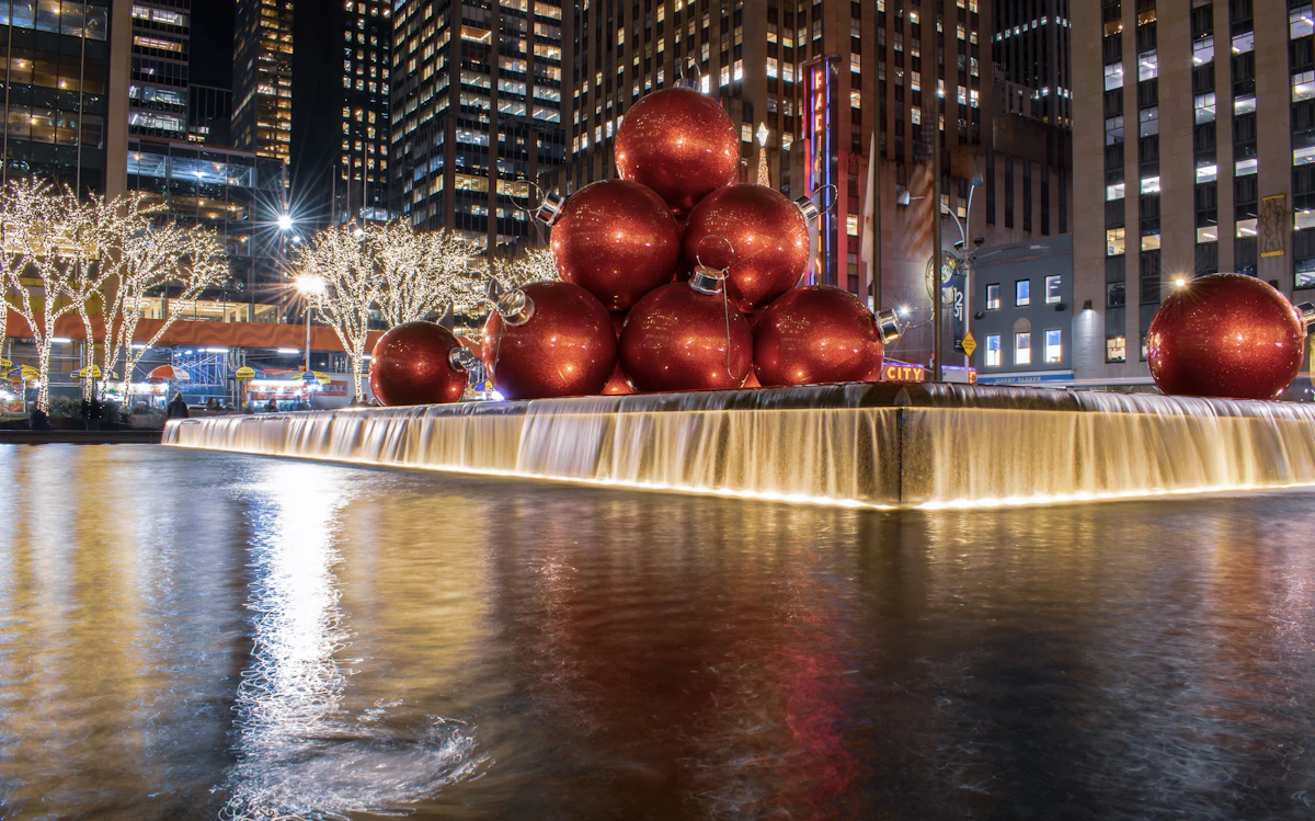 Giant red Christmas baubles on a lit fountain outside a Midtown office tower at night