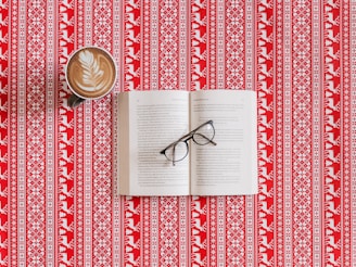 Open book on a wooden table with reading glasses and a cup of coffee.