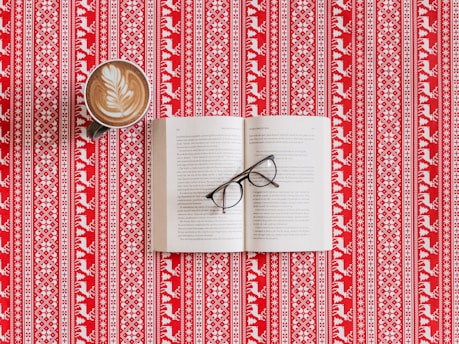 A finished printed book resting on a wooden table beside a cup of coffee and reading glasses.