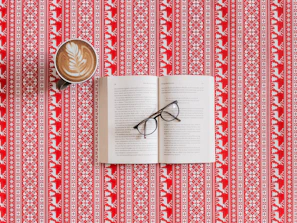 Stylish aviator sunglasses perched on an open book beside a cup of coffee.