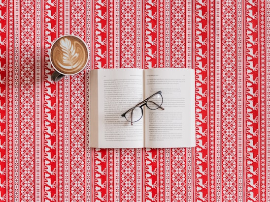 Open book on a wooden table with reading glasses and a cup of coffee.