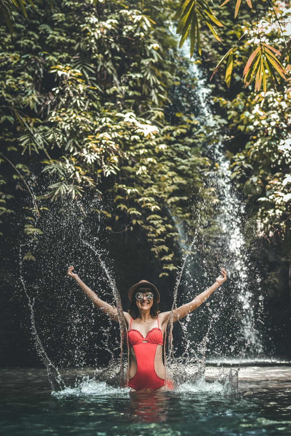 woman wearing red onepiece swimsuit in near the waterfall during daytime