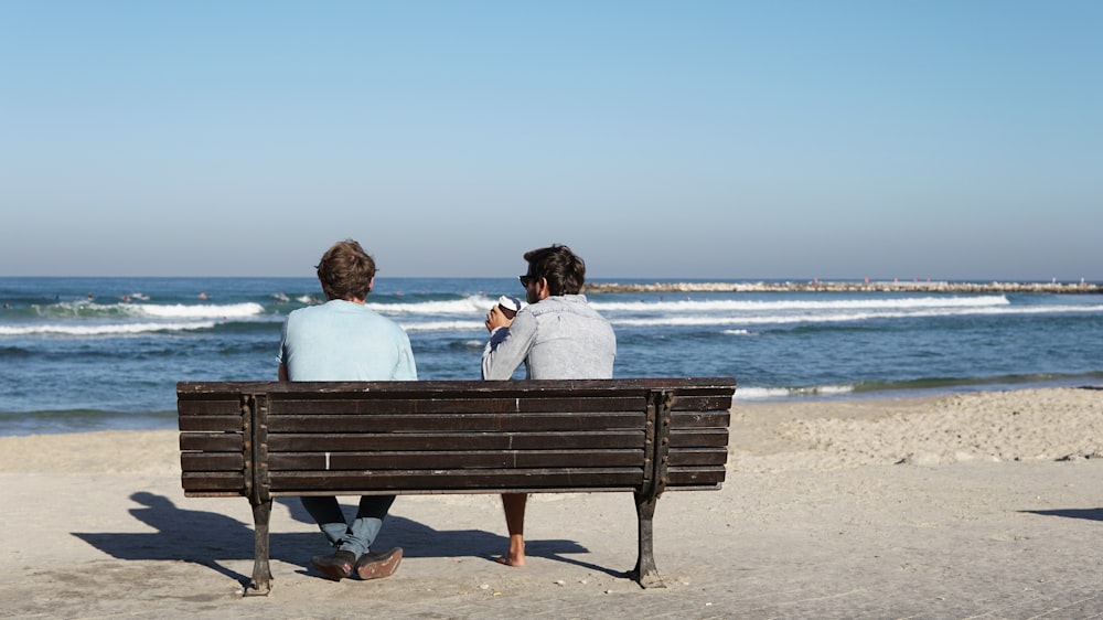 two men sitting on brown wooden bench on seashore