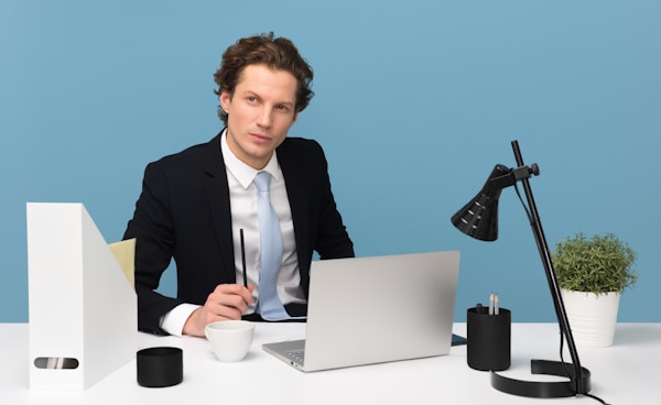 man sitting on chair beside laptop computer and teacup