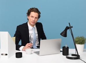 man sitting on chair beside laptop computer and teacup