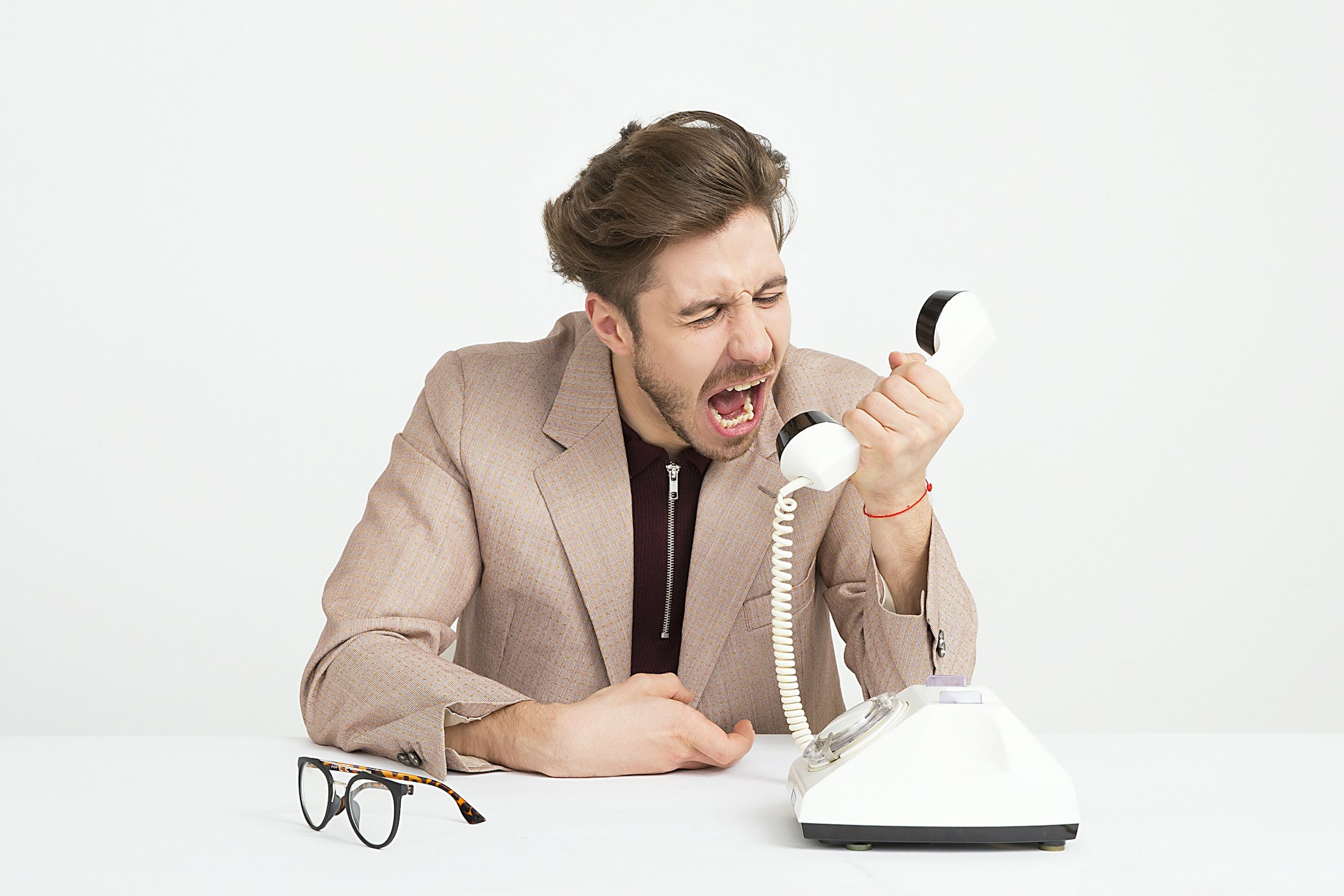 Brown haired man in beige suit yells into a white phone as if angry. A lot of business owners are skeptical of marketers - Inspired Idiots blog.