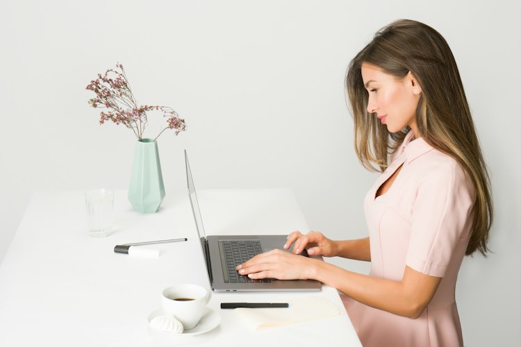 Freelancer typing on a laptop with a notebook of numbers beside them