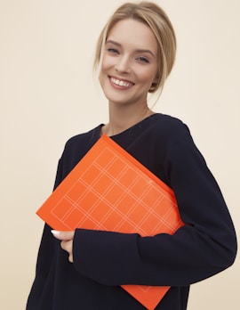 smiling woman standing while holding orange folder