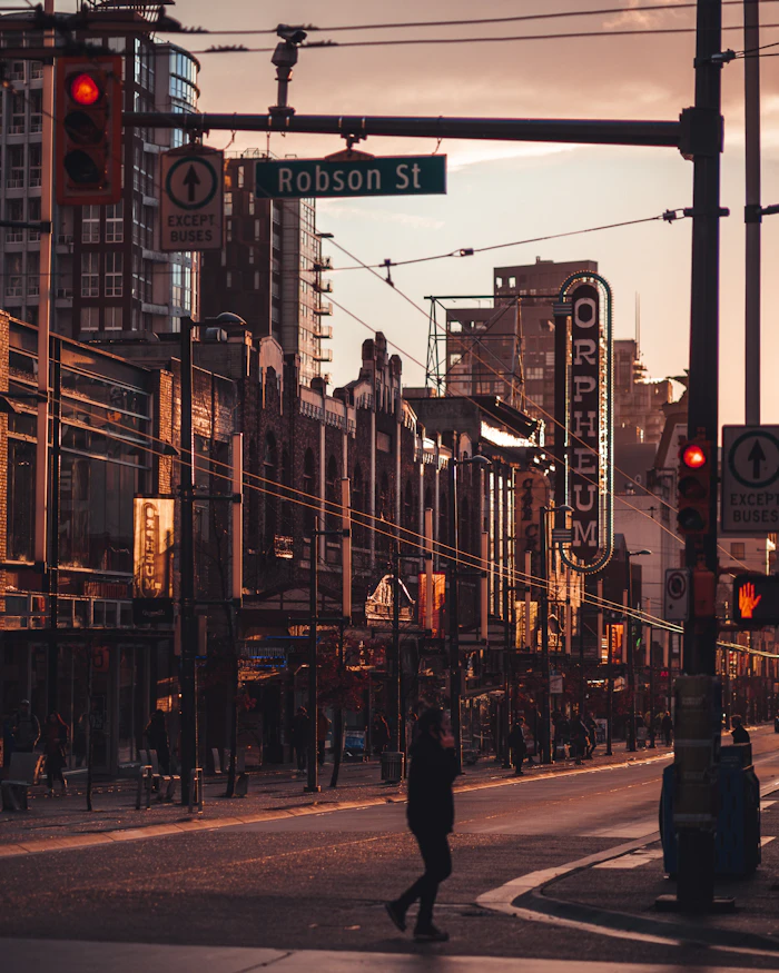 Robson Street in downtown Vancouver at golden hour, a pedestrian crossing under the street sign