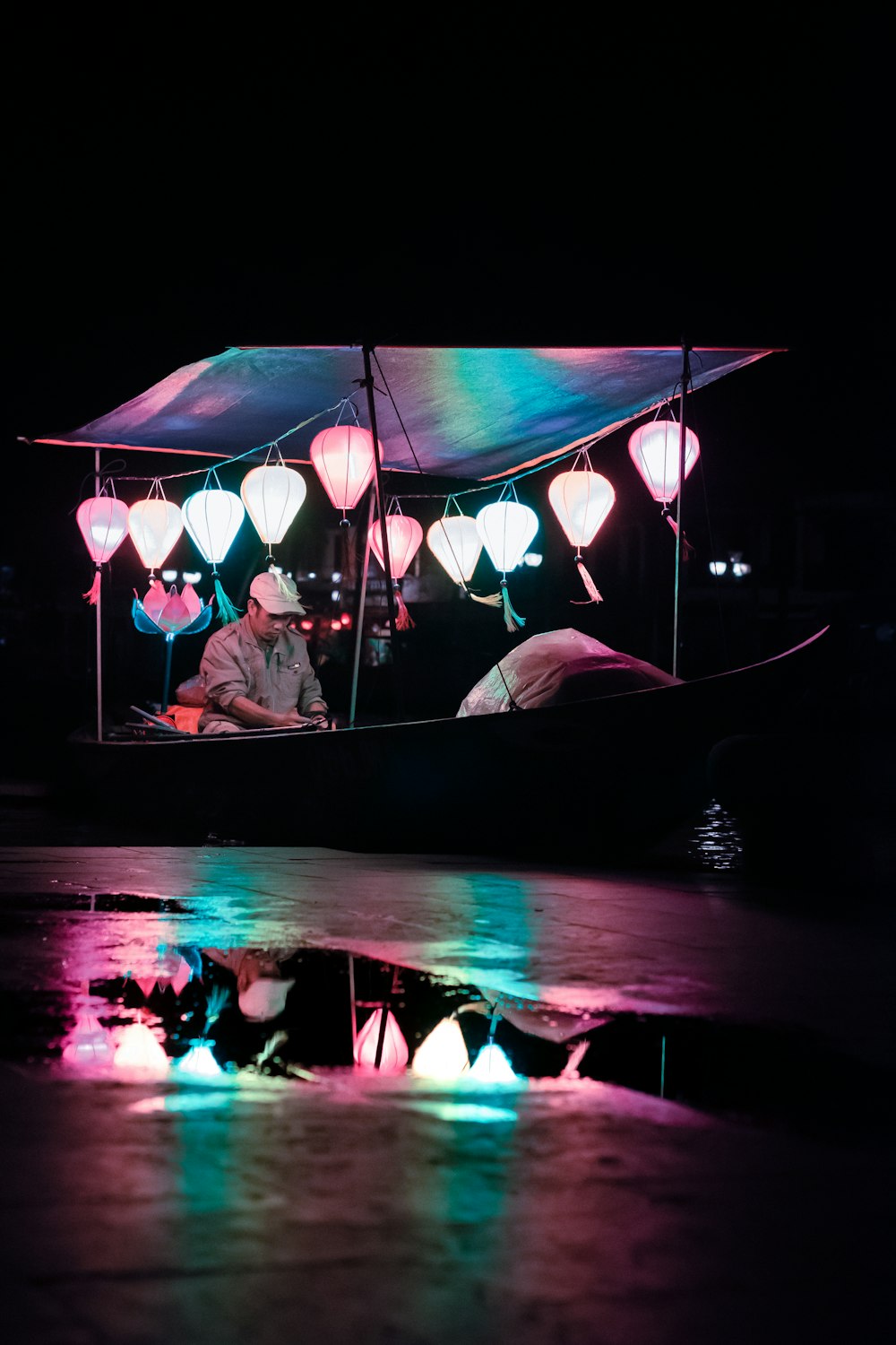 man riding boat with multicolored lanterns at night