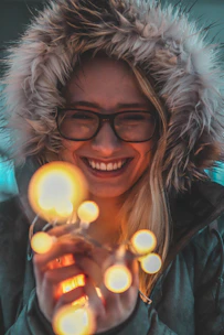 A smiling person holding a glowing, playful gadget in a cozy living room.