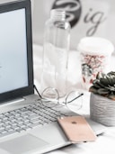 turned-on Asus laptop near eyeglasses, succulent plant, and empty clear glass bottle